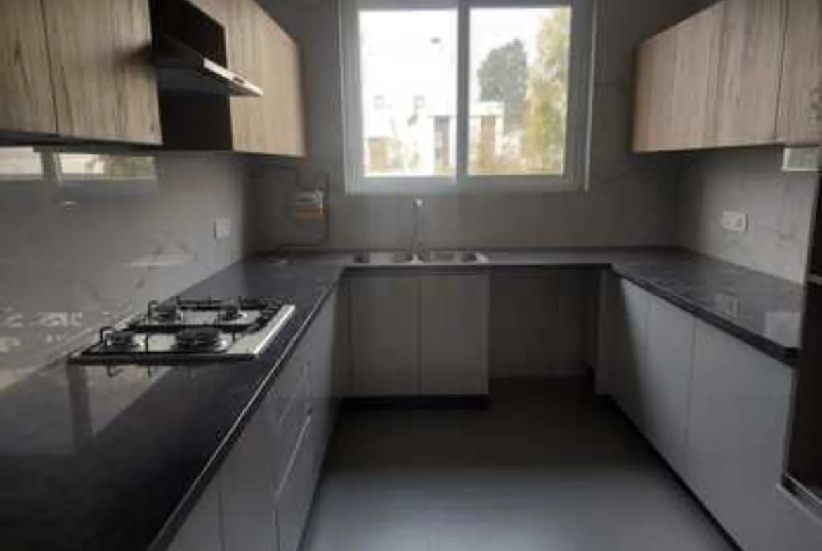 Modern kitchen in Greater Kailash-1 rental with light wood and gray cabinetry, dark granite countertops, and a gas cooktop.
