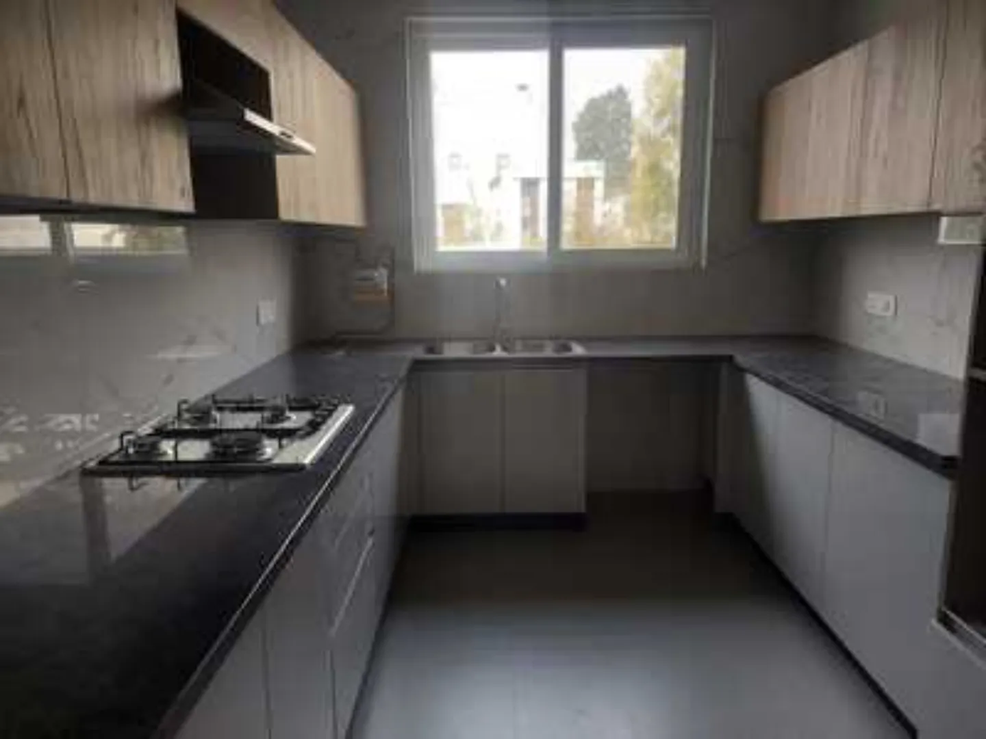 Modern kitchen in Greater Kailash-1 rental with light wood and gray cabinetry, dark granite countertops, and a gas cooktop.