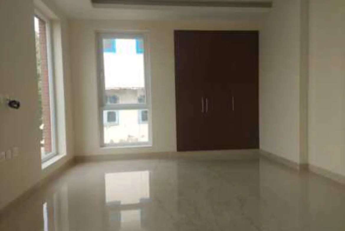 Interior shot of a room with polished flooring, two windows, and a dark wood wardrobe, rental in Greater Kailash-1.