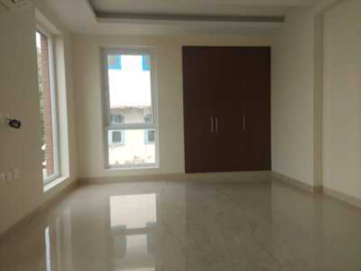 Interior shot of a room with polished flooring, two windows, and a dark wood wardrobe, rental in Greater Kailash-1.