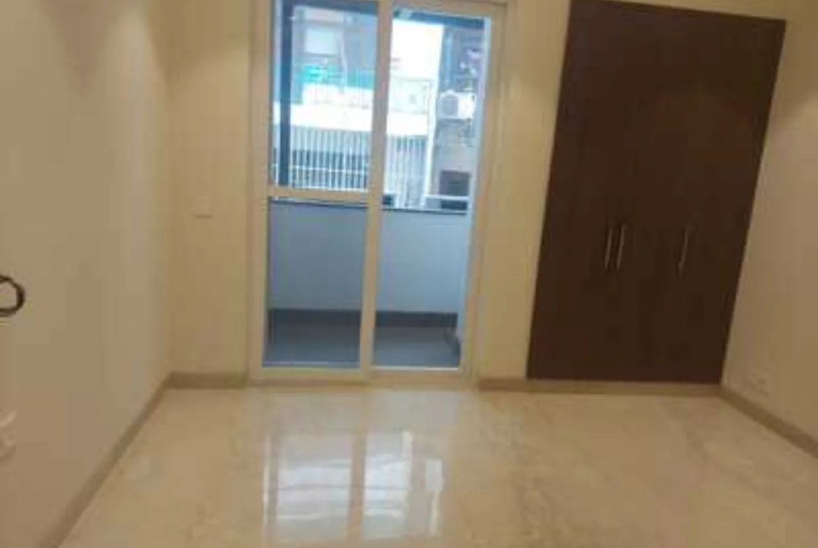 Bright room with polished tile flooring, balcony access through sliding glass doors, and a dark brown built-in wardrobe, Greater Kailash-1 rental.