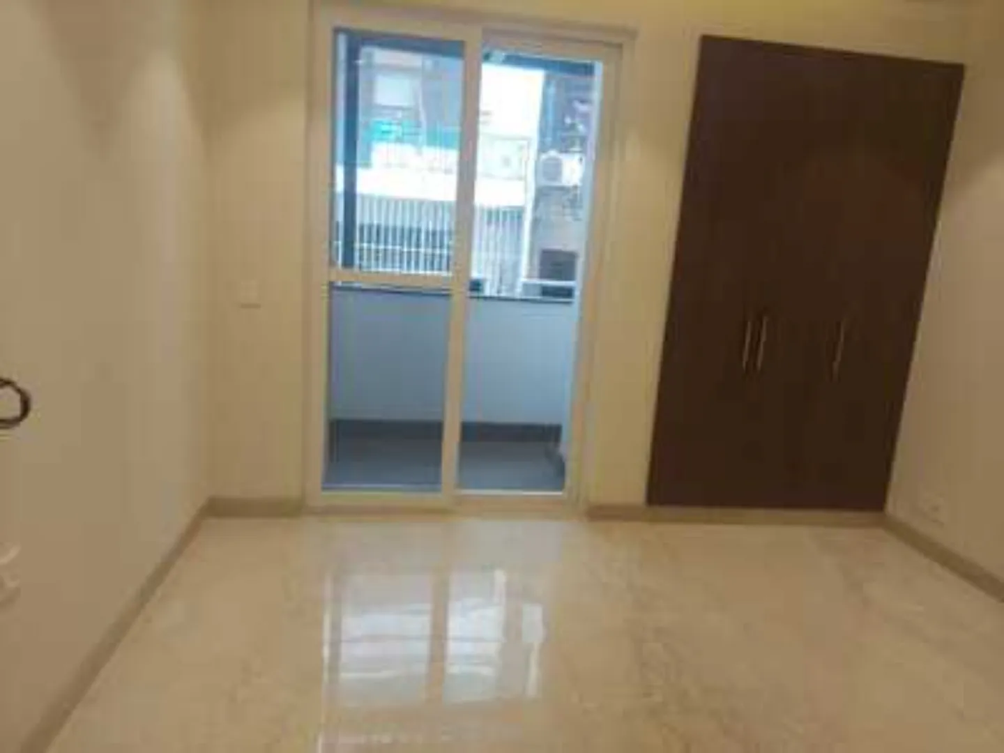 Bright room with polished tile flooring, balcony access through sliding glass doors, and a dark brown built-in wardrobe, Greater Kailash-1 rental.