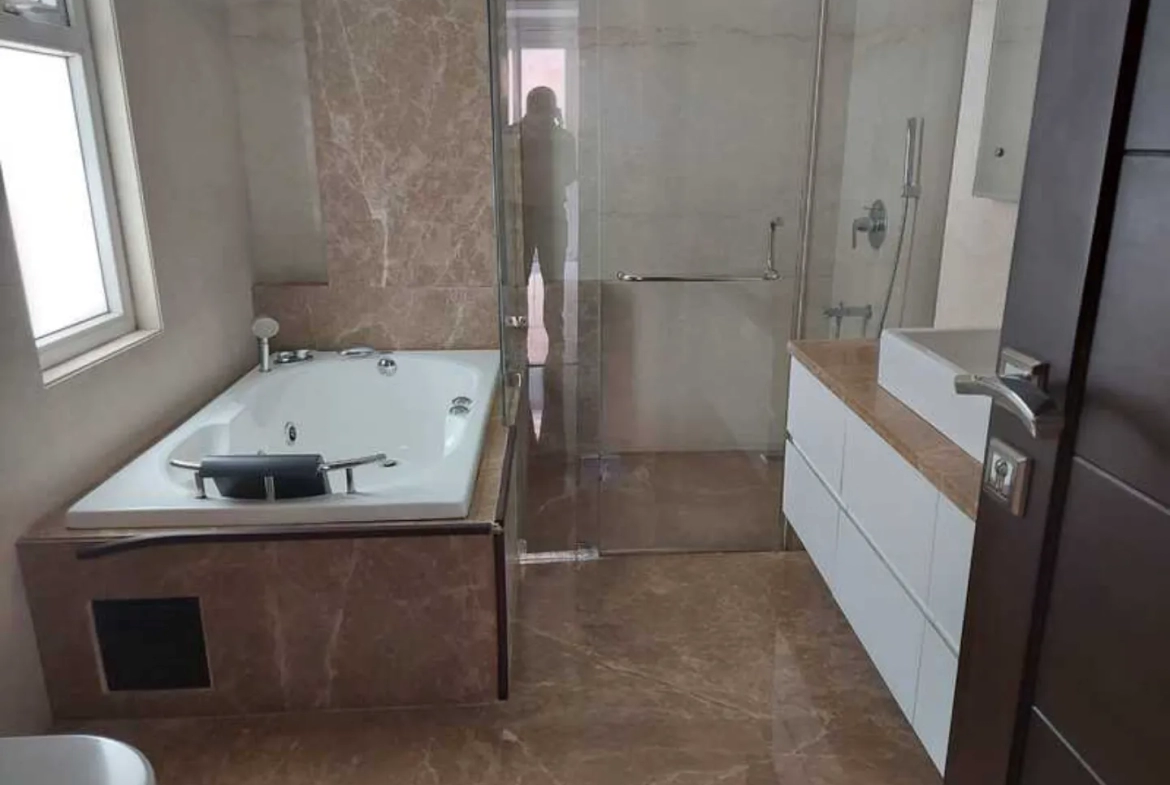 "Bathroom with bathtub, glass shower, and vanity, modern design, South Delhi rental."