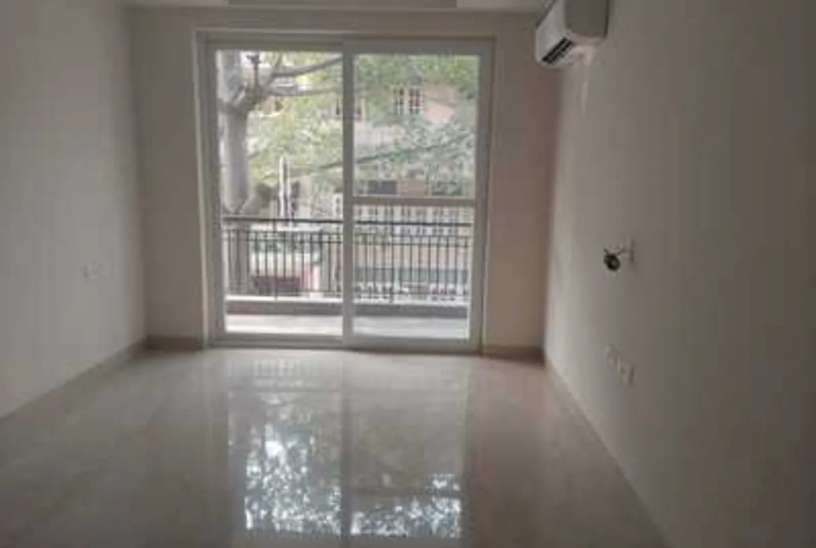 Empty room with sliding glass doors to a balcony, polished floor tiles, and AC unit in a rental apartment in Greater Kailash-1, South Delhi.